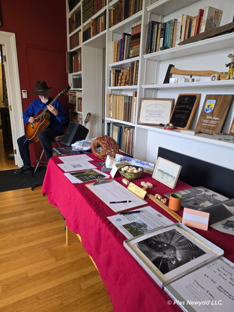 A long table with a red tablecloth with various items laid on it, and a gentlemen playing guitar in the background.